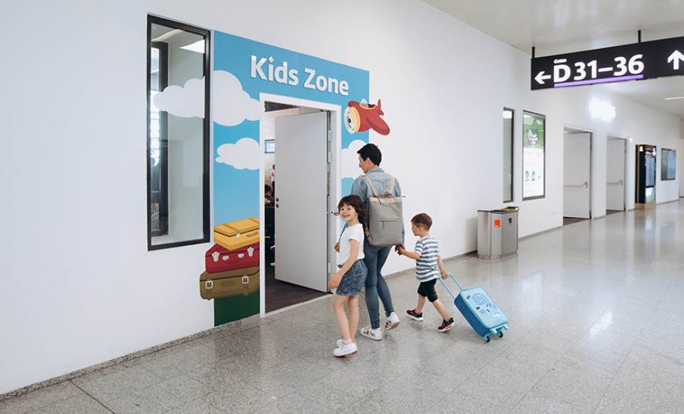 Familie betritt die farbenfrohe Kids Zone am Flughafen, nahe den Gates D31–36