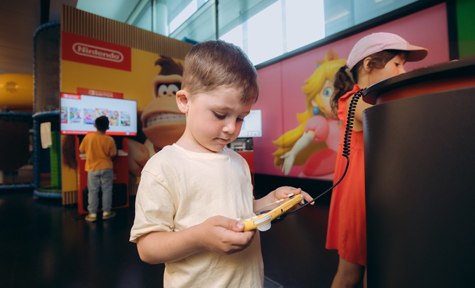 Kind spielt mit Handheld-Konsole in Nintendo-Spielbereich am Flughafen