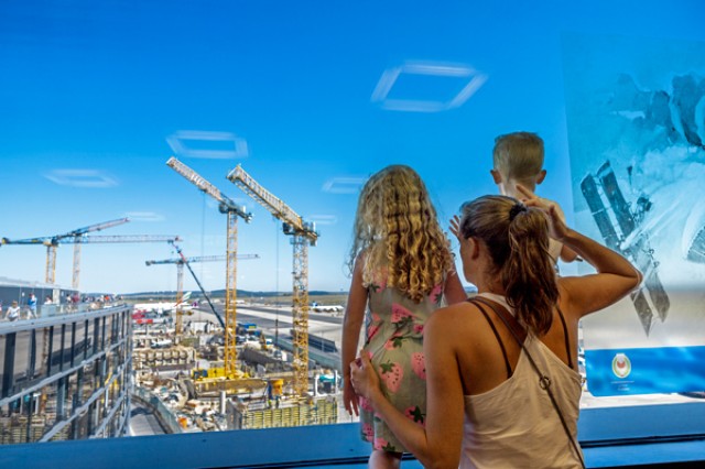 Mother and children watching airport construction through glass.